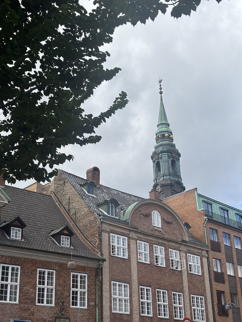 A historic brick building with a tall spire framed by trees