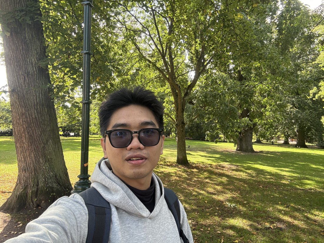 Thanh-Nhan taking a photograph in a green park with sunlit trees