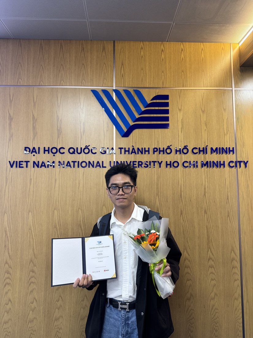Thanh-Nhan with his scholarship certificate and flowers beside the VNU-HCM emblem